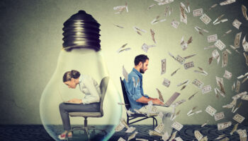 woman-sitting-inside-electric-lamp-using-working-on-computer-in-corporate-office-next-to-young-entrepreneur-man-under-money-rain